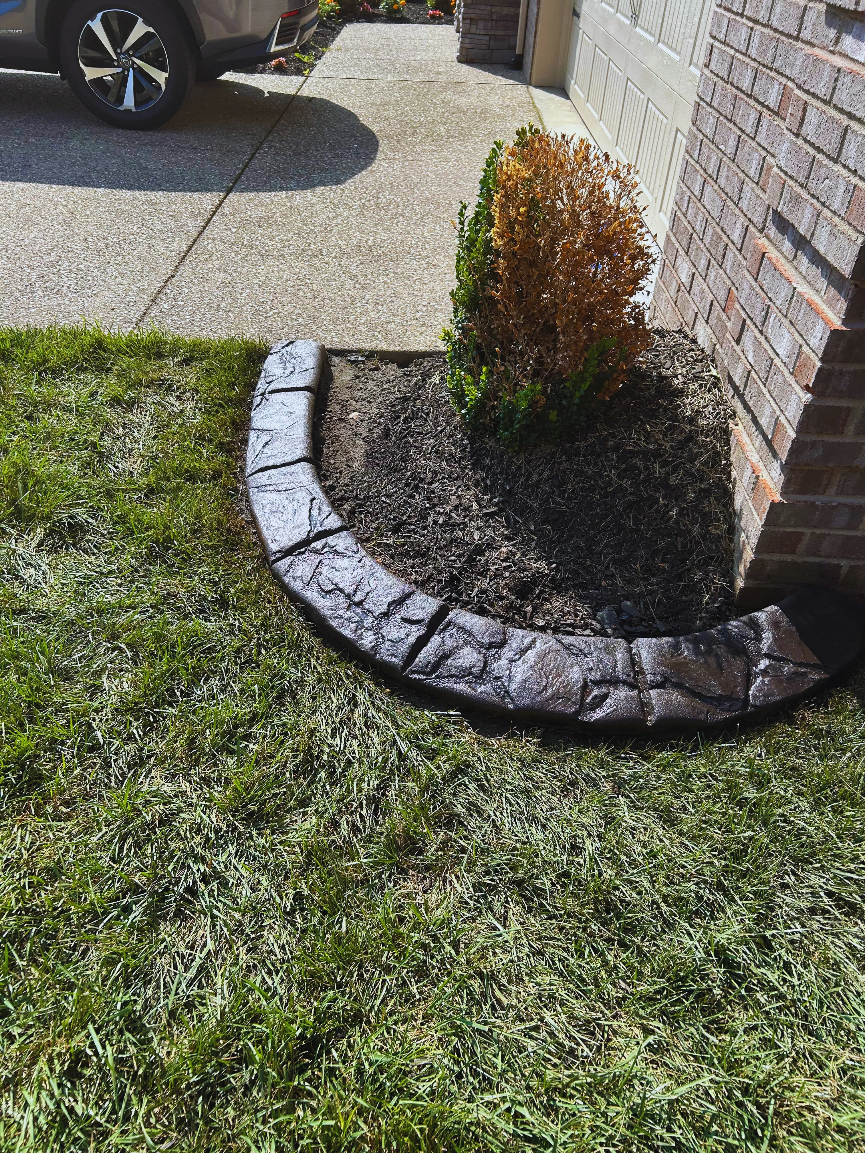Dark stamped concrete curbing curving along a driveway in front of a brick home