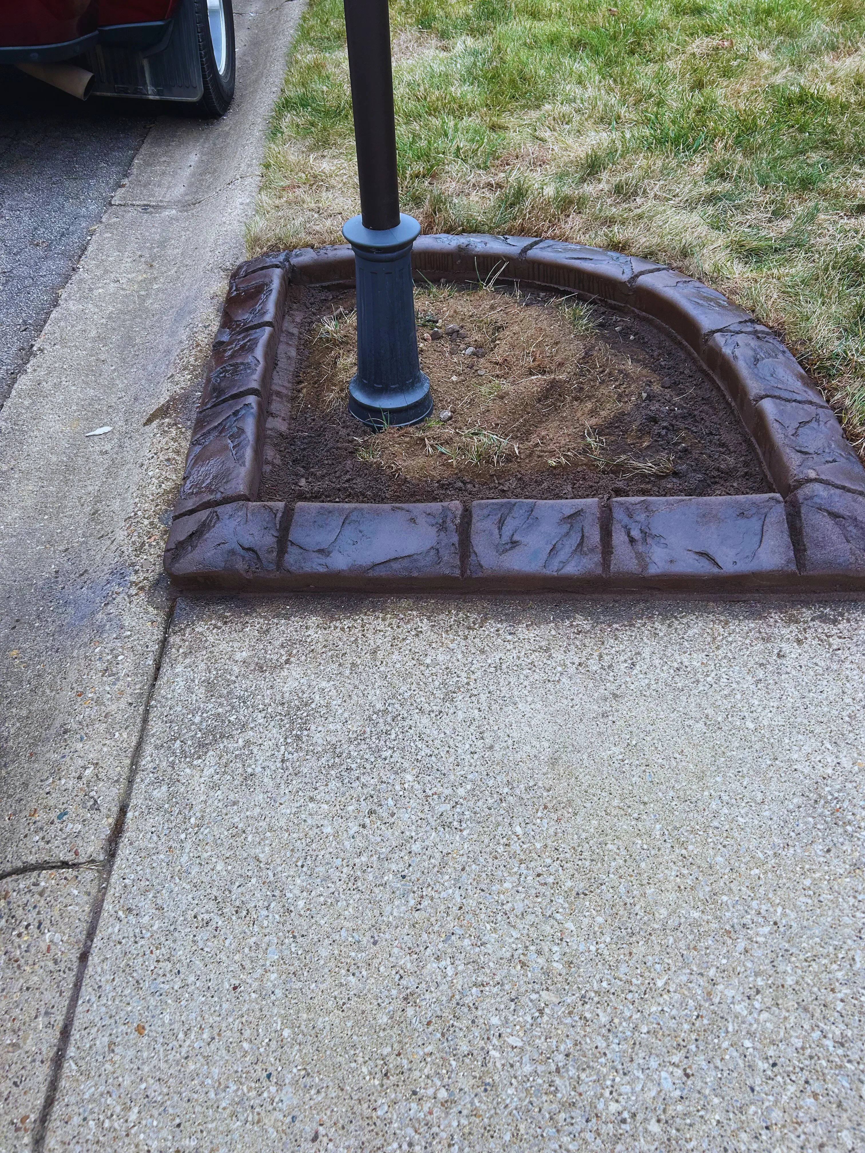 A small angular stamped-concrete bed around a lamppost beside a driveway