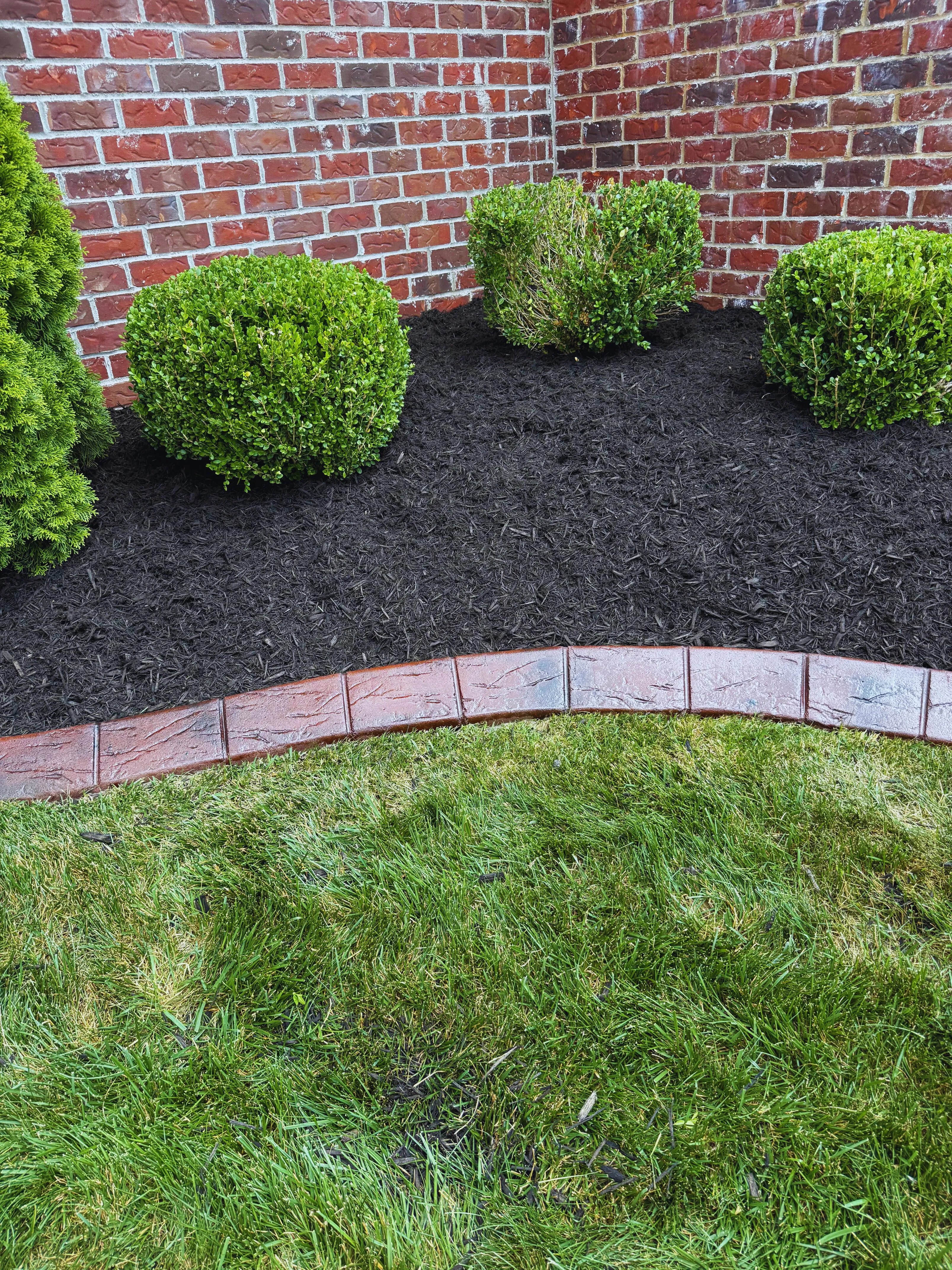 Brick-red stamped concrete curbing wrapping a mulched bed against a brick house facade