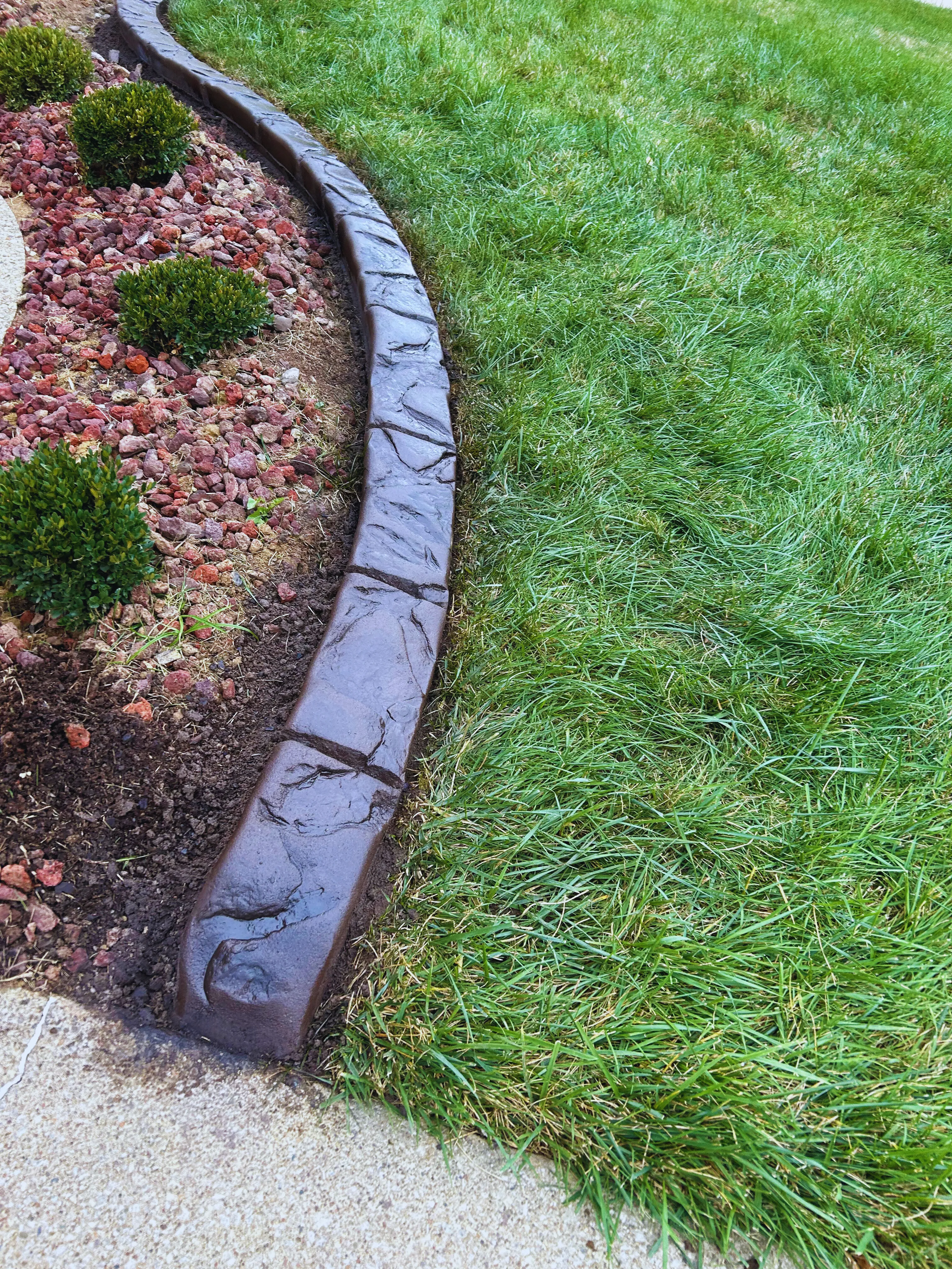 Stamped concrete landscape curbing curving between a red-rock mulched bed and the front lawn