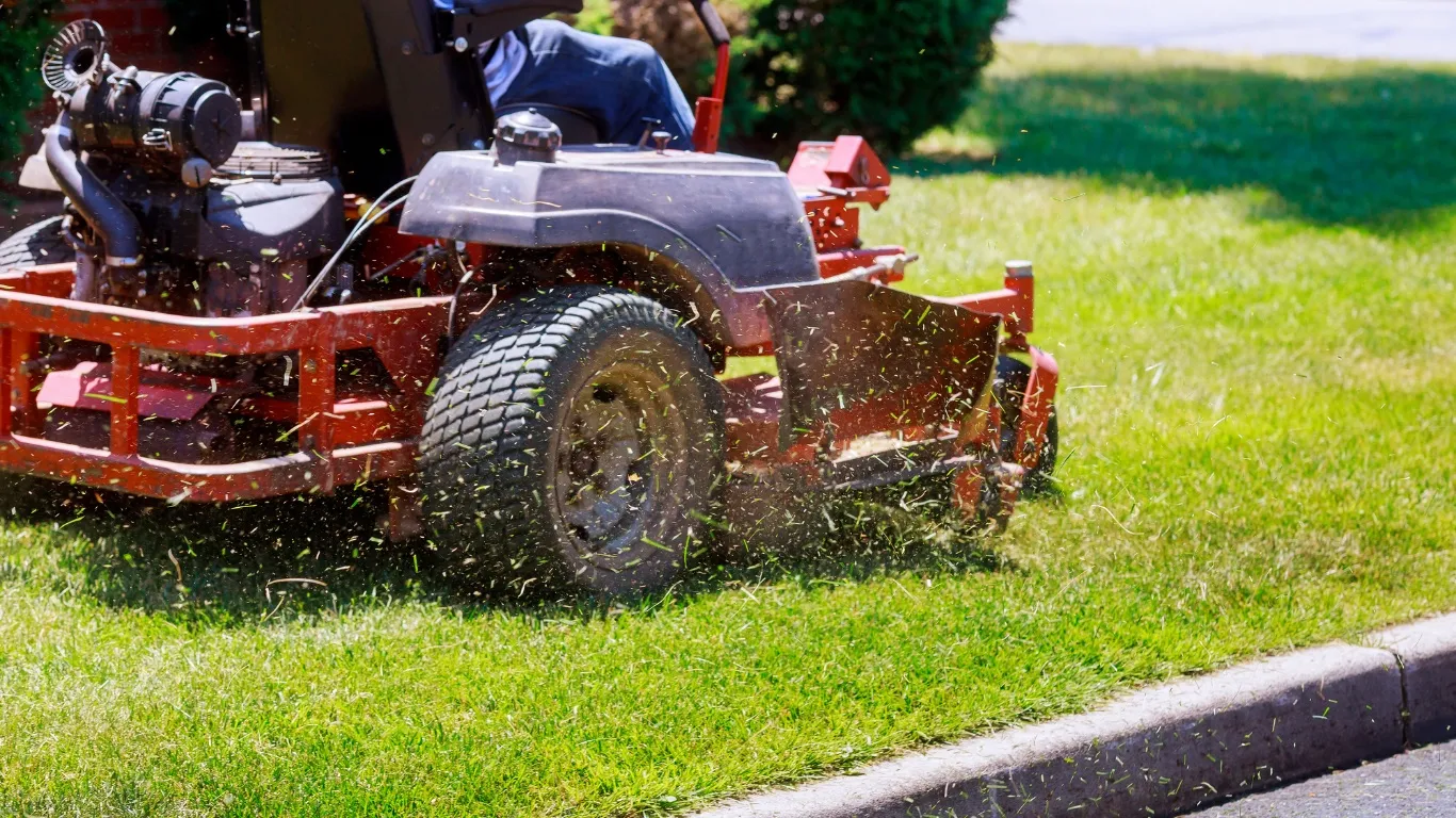 A zero-turn mower cutting a healthy green lawn along a curbed driveway
