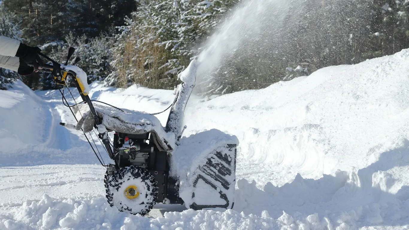 A two-stage snow blower clearing a snow-covered driveway in winter